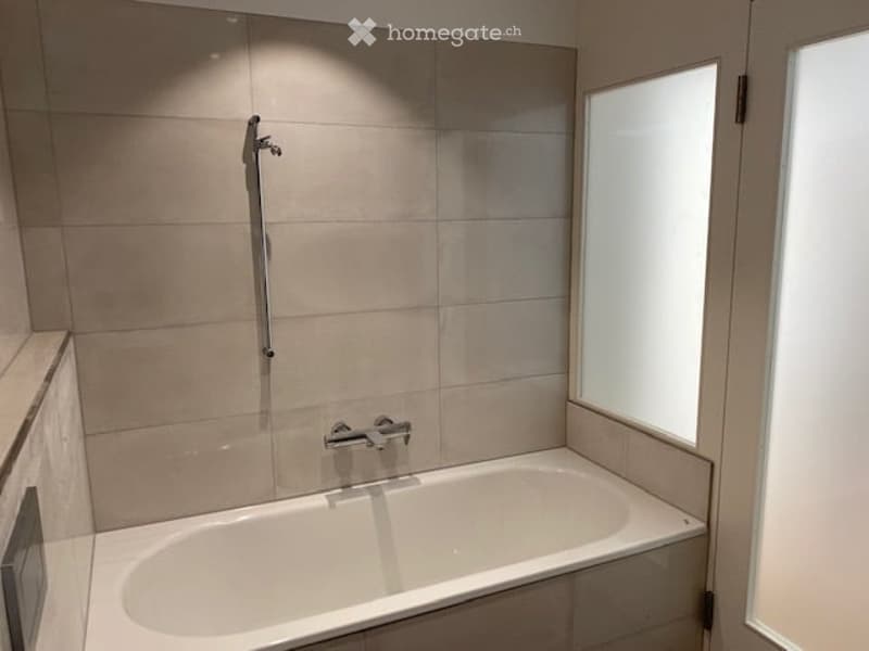 Modern bathroom with a bathtub, tiled walls, and a window providing natural light.