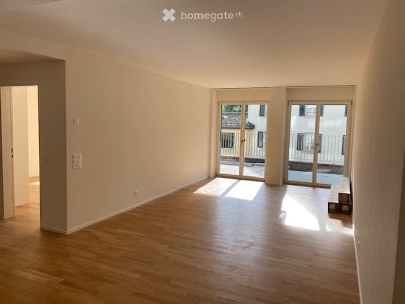 Empty room with wooden flooring, large sliding glass doors leading to a balcony, and neutral-colored walls.