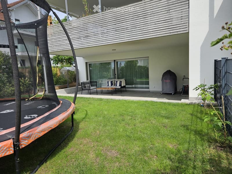 Garden with a trampoline, modern house with large windows, patio furniture, and a covered grill.