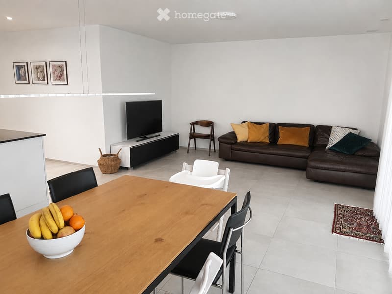 Modern living and dining area with a brown leather sofa, wooden dining table, black chairs, TV stand, and decorative items.