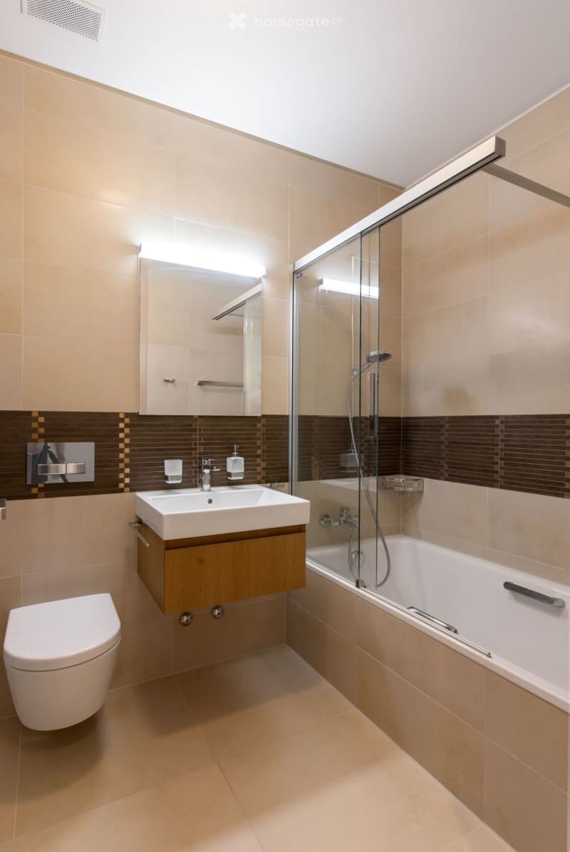 Modern bathroom with beige tiles, a white sink, toilet, bathtub, and a glass-enclosed shower area.