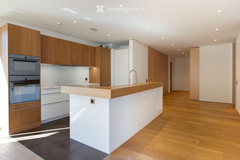 Modern kitchen with wooden cabinets, white countertops, built-in oven, and a central island with a wooden top.