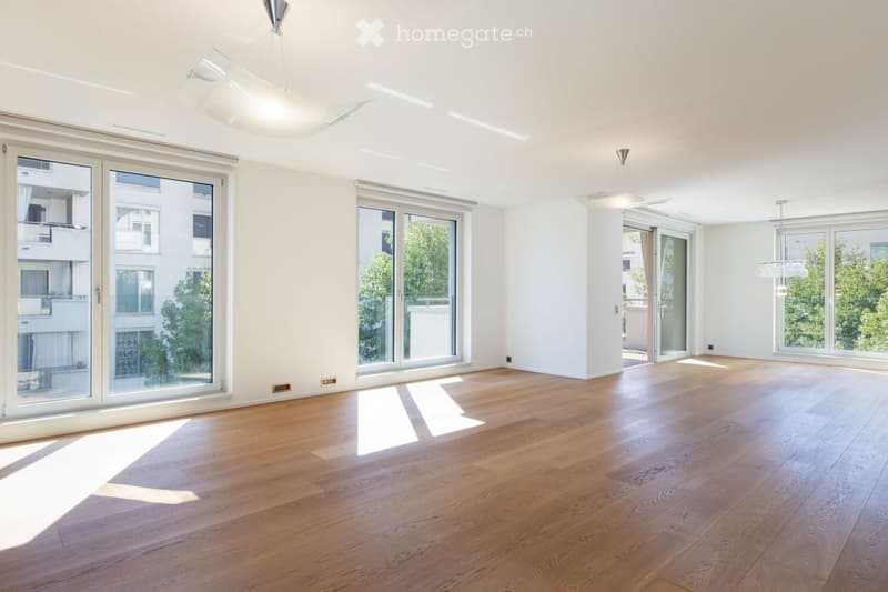 Empty room with wooden flooring, large windows, and modern ceiling lights.