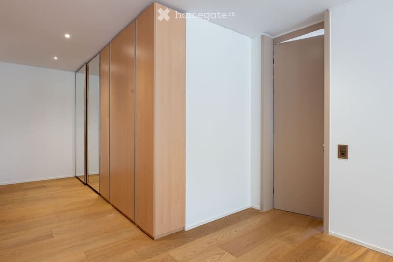 Empty room with light wooden flooring, white walls, and a large mirrored wardrobe unit on one side.