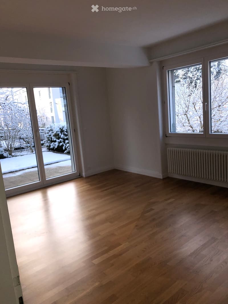Empty room with wooden flooring, large windows, and sliding glass doors leading to a snowy outdoor area.
