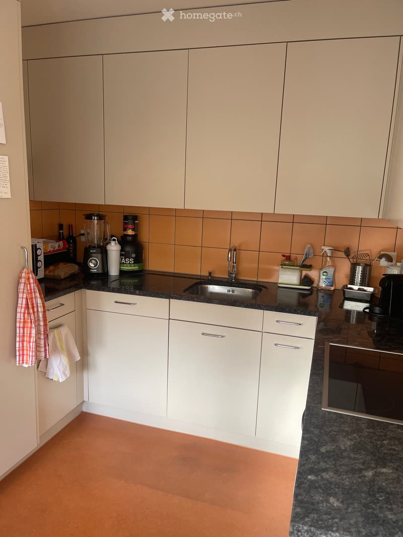 Modern kitchen with white cabinets, granite countertop, stainless steel sink, and various appliances including a blender and oven.