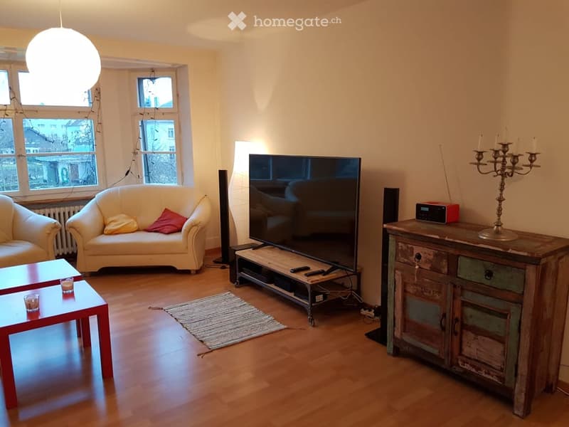 Living room with light-colored sofa, armchair, coffee table, television, speakers, and a wooden cabinet with a candelabra on top.