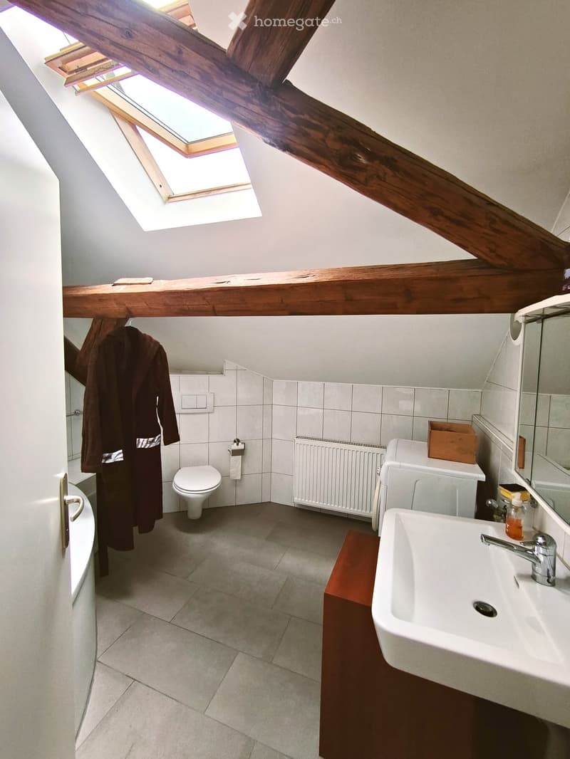 Bathroom with a toilet, sink, bathtub, and a wooden shelf. Features exposed wooden beams and a skylight window.