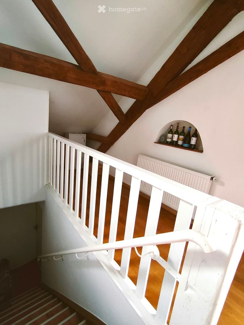 Staircase with wooden beams, white railing, and a small shelf holding several bottles of wine.