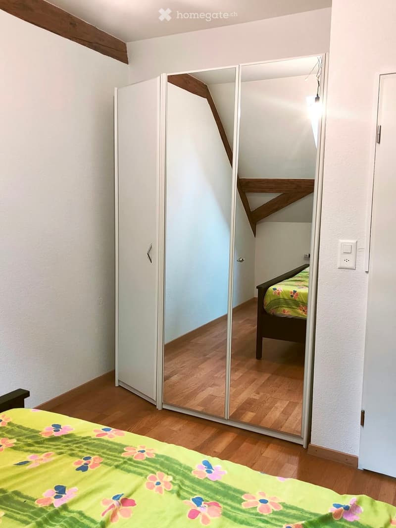 A cozy bedroom with wooden flooring, a large mirror reflecting the bed, and a colorful bedspread.