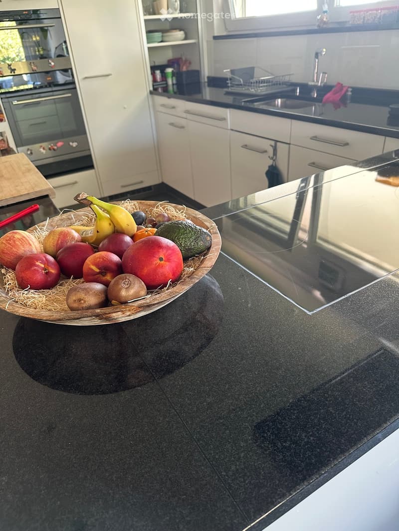 Modern kitchen with white cabinets, black countertops, and a bowl of fruit on the counter.