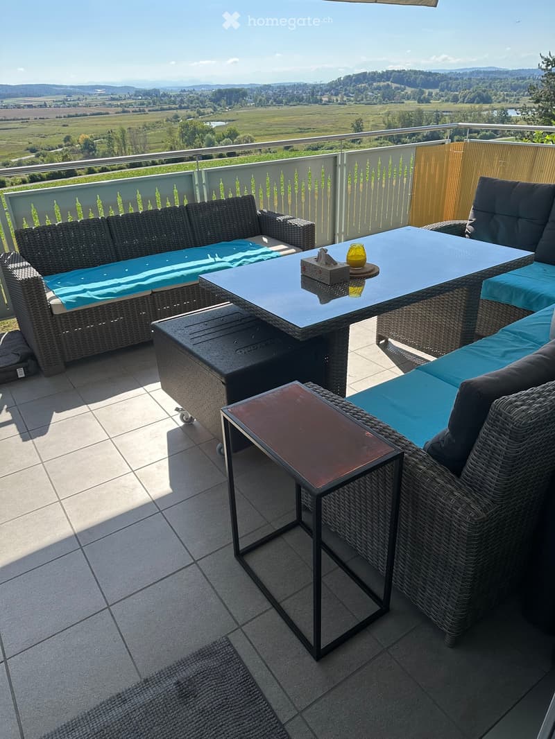 Balcony with wicker furniture, including a sofa, table, and chairs, set against a scenic countryside view.