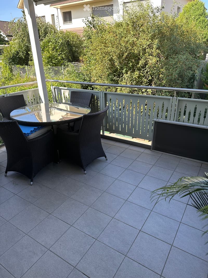 Balcony with tiled floor, metal railing, and outdoor furniture including a table and chairs.