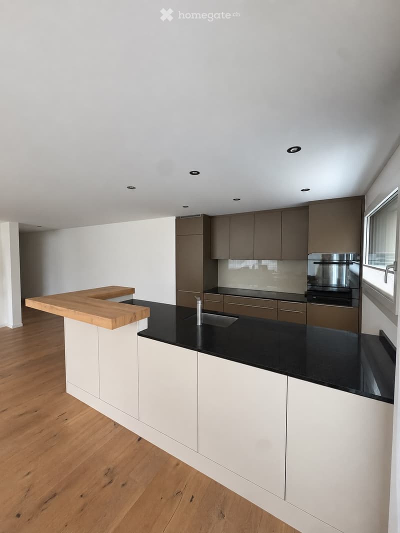 Modern kitchen with white and grey cabinets, black countertops, wooden island, and stainless steel appliances.