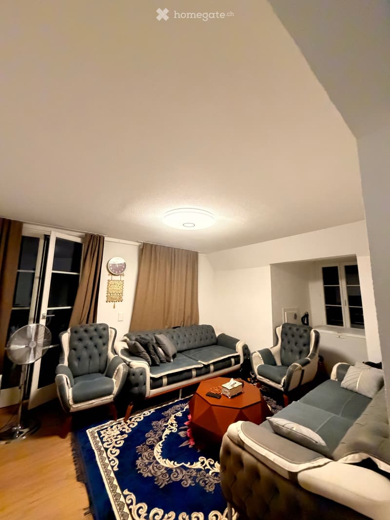 Living room with a blue sofa, two matching armchairs, a coffee table, a fan, and a decorative rug.