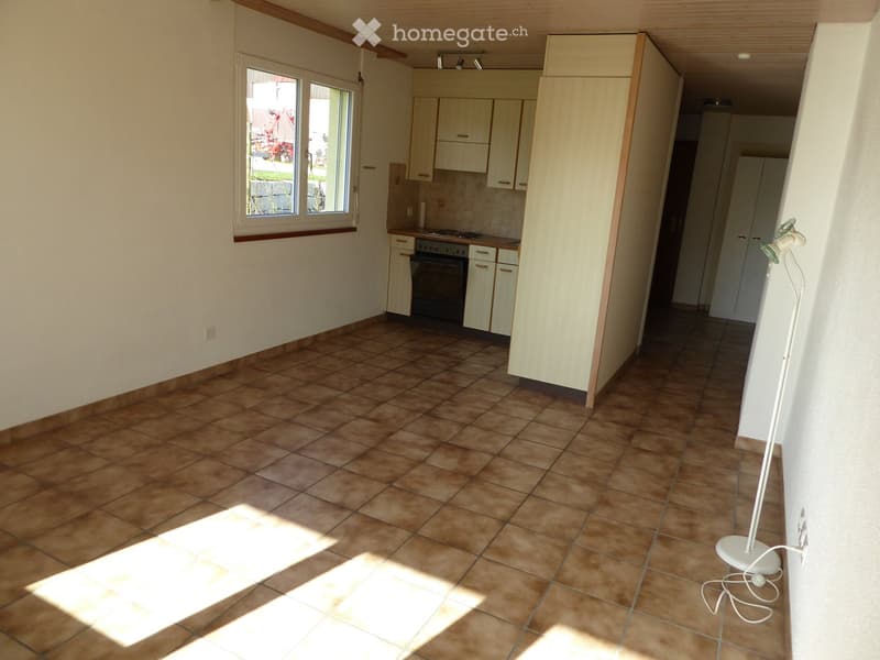 Empty kitchen with tiled floor, white cabinets, and an oven. Natural light streams in from a window on the left.