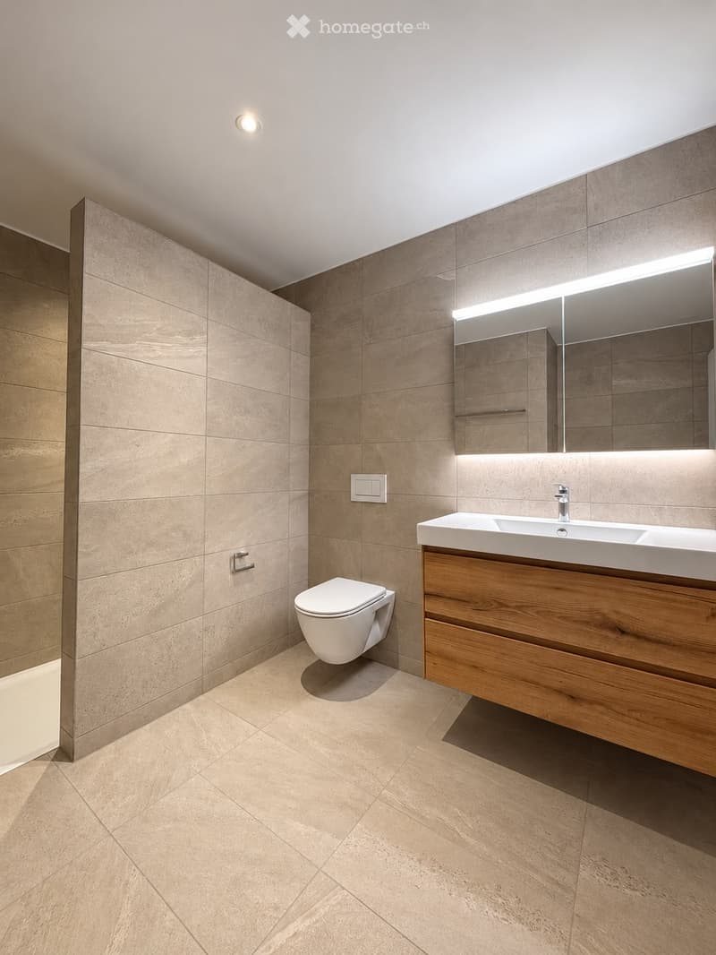Modern bathroom with beige tiles, a floating wooden sink cabinet, a sleek mirror with integrated lighting, and a toilet.
