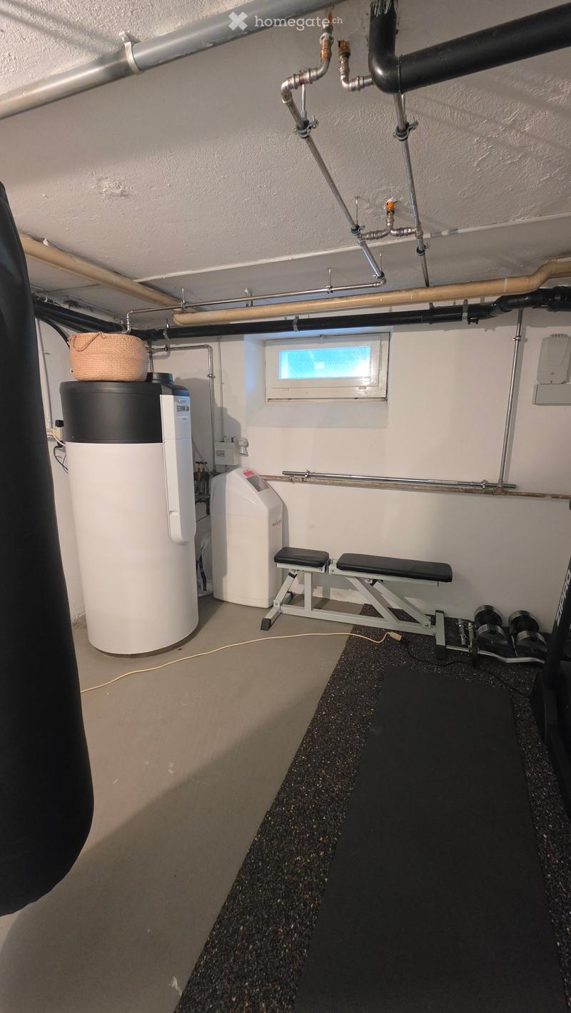 Utility room with water heater, bench, stool, and wicker basket. Exposed pipes and a small window are visible.
