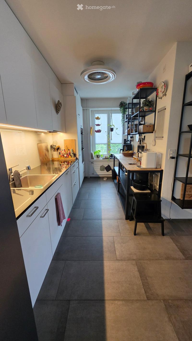 Modern kitchen with white cabinets, dark countertops, and a central island. Features include a sink, stove, refrigerator, microwave, and various kitchen appliances and utensils.