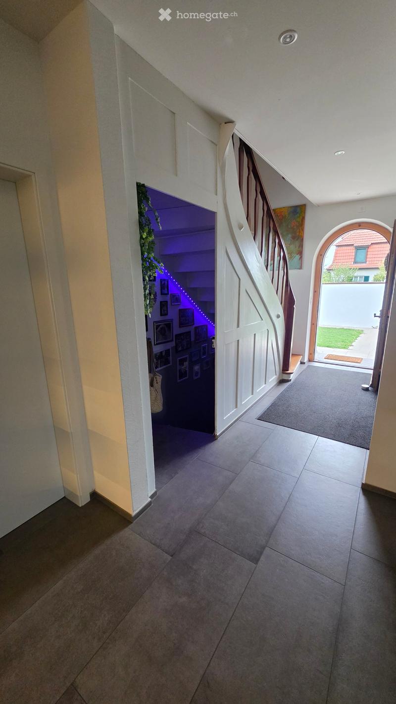 Hallway with tiled floor, staircase leading upwards, framed pictures on wall, and an open doorway to the garden.