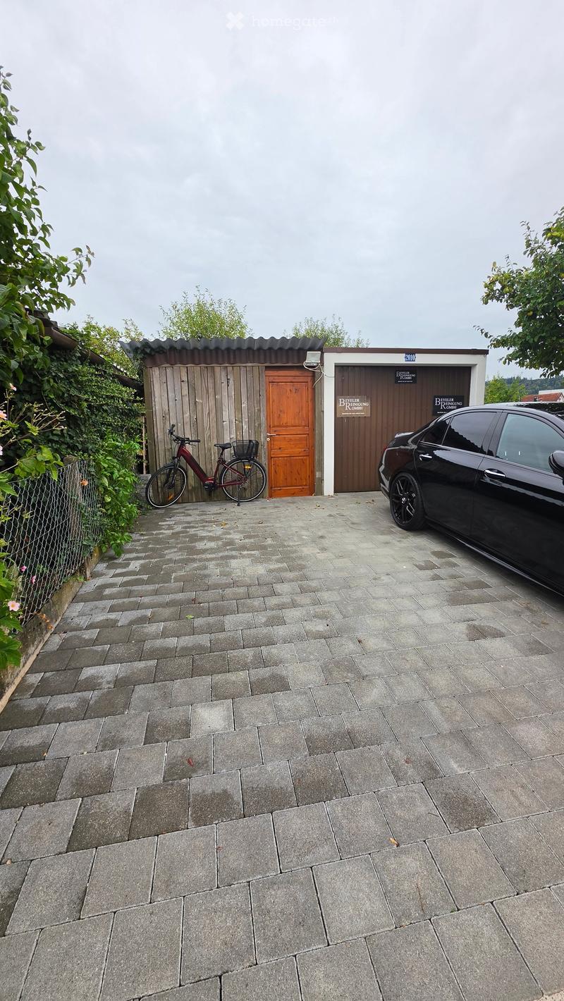 Paved outdoor area with a garage, bicycle, and parked car.