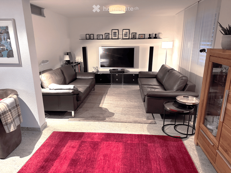 Modern living room with two brown leather sofas, a coffee table, a television, and decorative items on shelves.