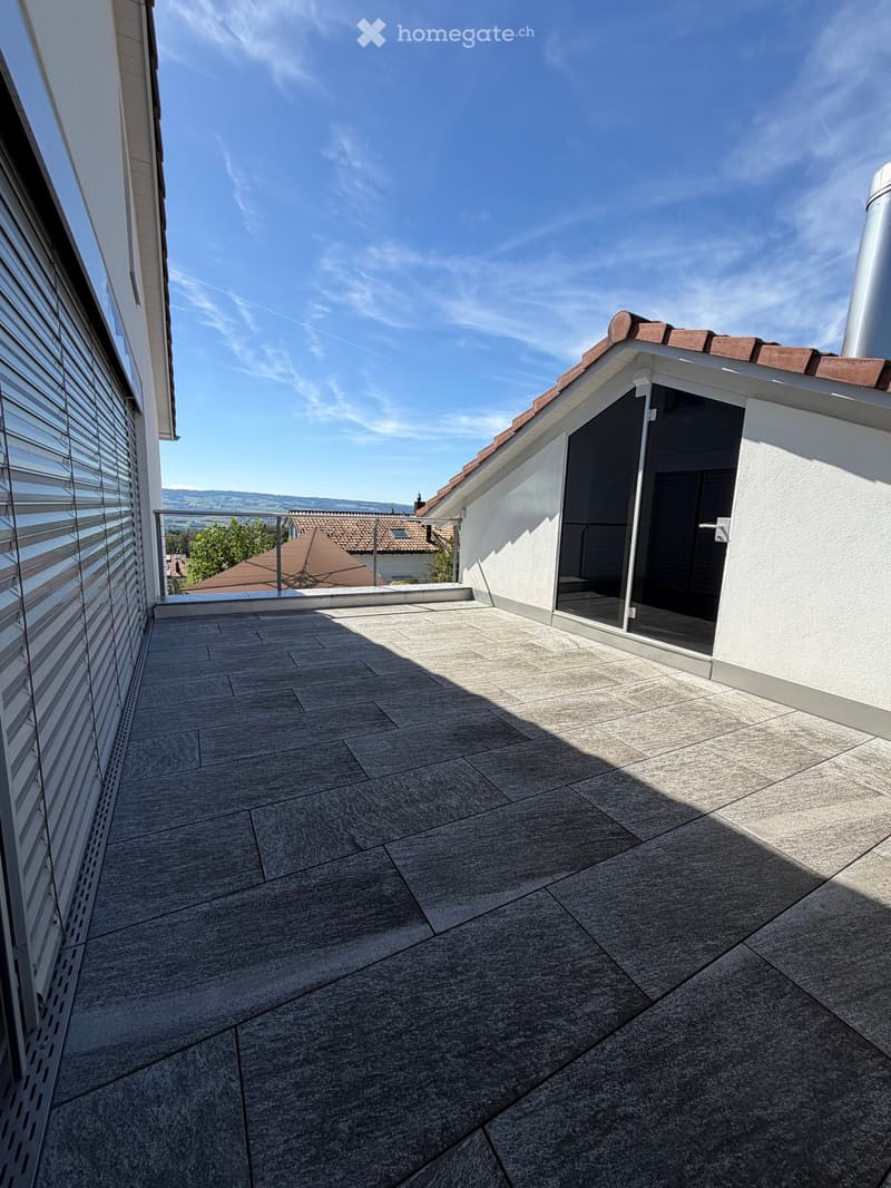 Roof terrace with grey stone tiles, white walls, and a view of the surrounding area.