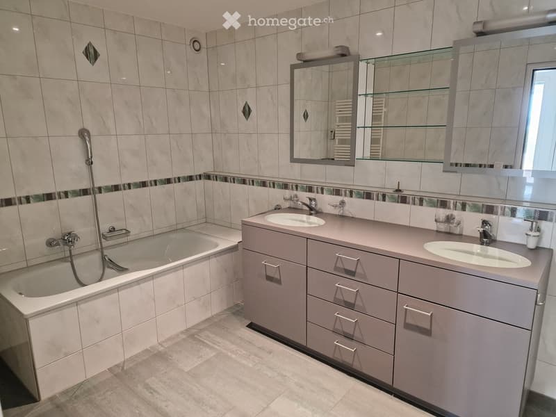 Modern bathroom with a bathtub, double sink vanity, mirrored cabinet, and tiled walls.