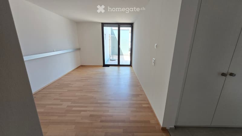 Empty hallway with wooden flooring, white walls, and a sliding glass door leading to another room.
