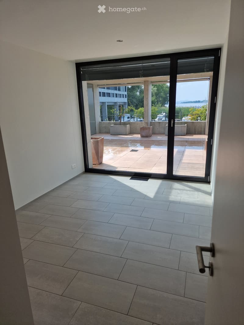 Hallway with tiled floor, large sliding glass door leading to a tiled outdoor area with planters and a view of the sea.