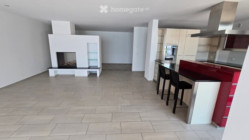 Modern open-plan space with a fireplace, kitchen island, and stools, featuring sleek cabinets and a stainless steel range hood.