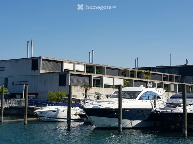 Marina with several docked yachts and boats, surrounded by modern buildings with large windows and balconies.