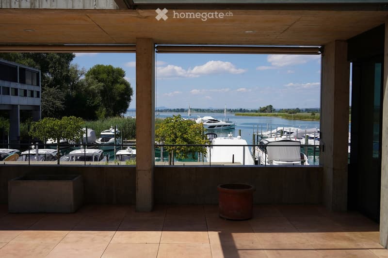 Balcony with tiled floor, wooden ceiling, overlooking a marina with several boats and a body of water.