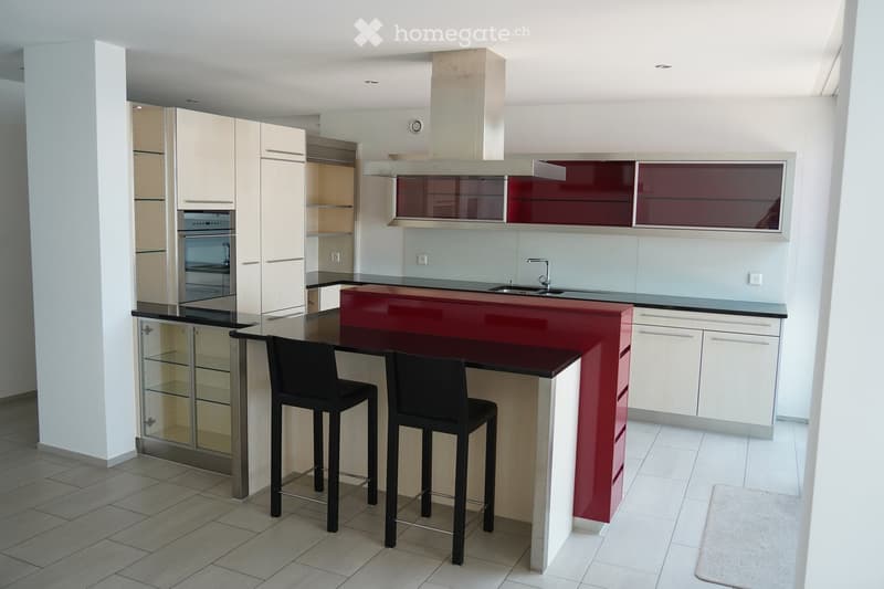 Modern kitchen with white and red cabinets, a central island with bar stools, an oven, and a sink.