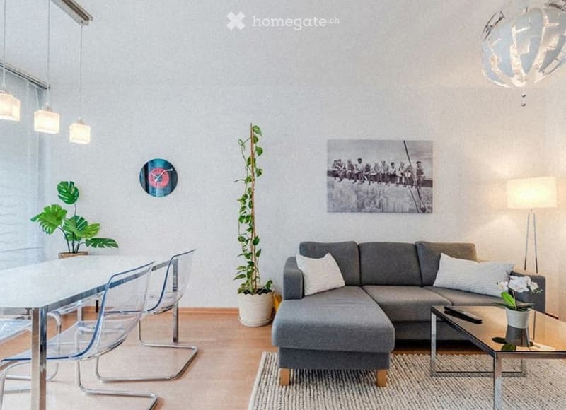 Modern living room with grey sectional sofa, coffee table, dining table with chairs, potted plants, floor lamp, and artwork on the wall.