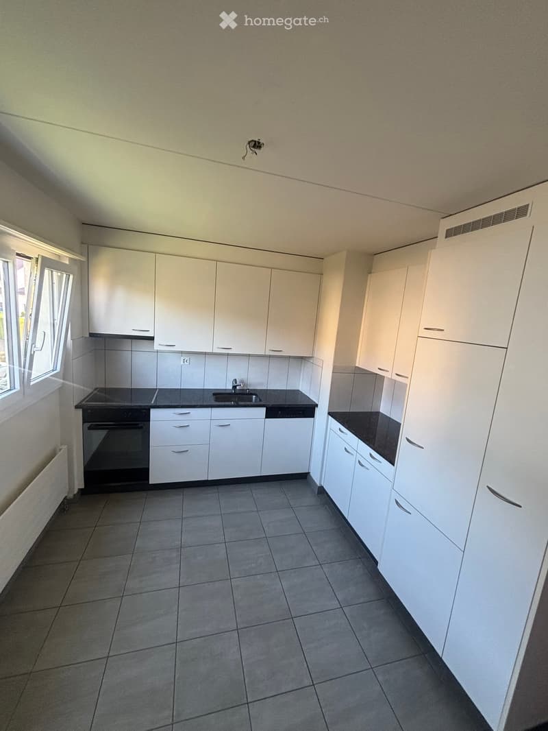 Empty kitchen with white cabinets, black countertops, and tiled flooring. Features include a sink, stove, and built-in oven.
