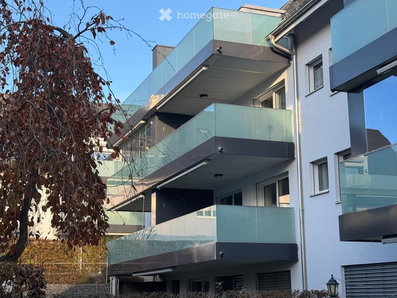 Modern multi-story building with glass balconies and sleek design, featuring multiple levels with large windows and contemporary architecture.