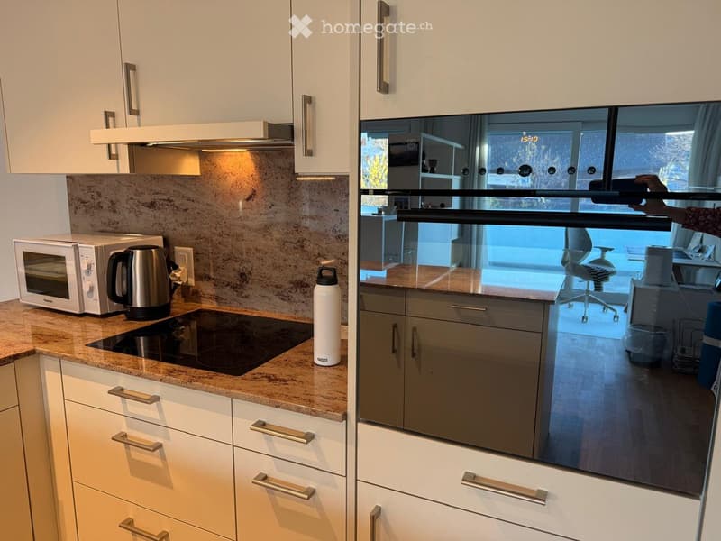 Modern kitchen with white cabinets, granite countertop, induction stove, microwave, electric kettle, and a stainless steel bottle on the counter.