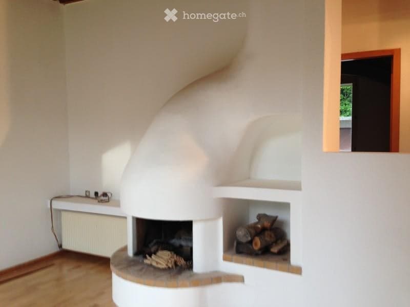 Modern living room with a white, curved fireplace and a built-in wood storage compartment. The room features light wooden flooring and white walls.