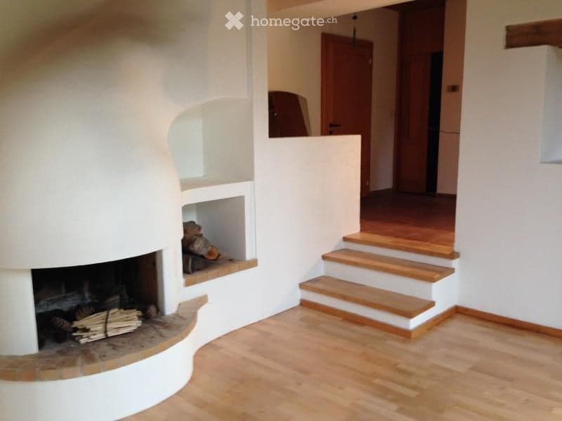Modern living room with a built-in white fireplace, wooden staircase leading to an upper level, and light wooden flooring.