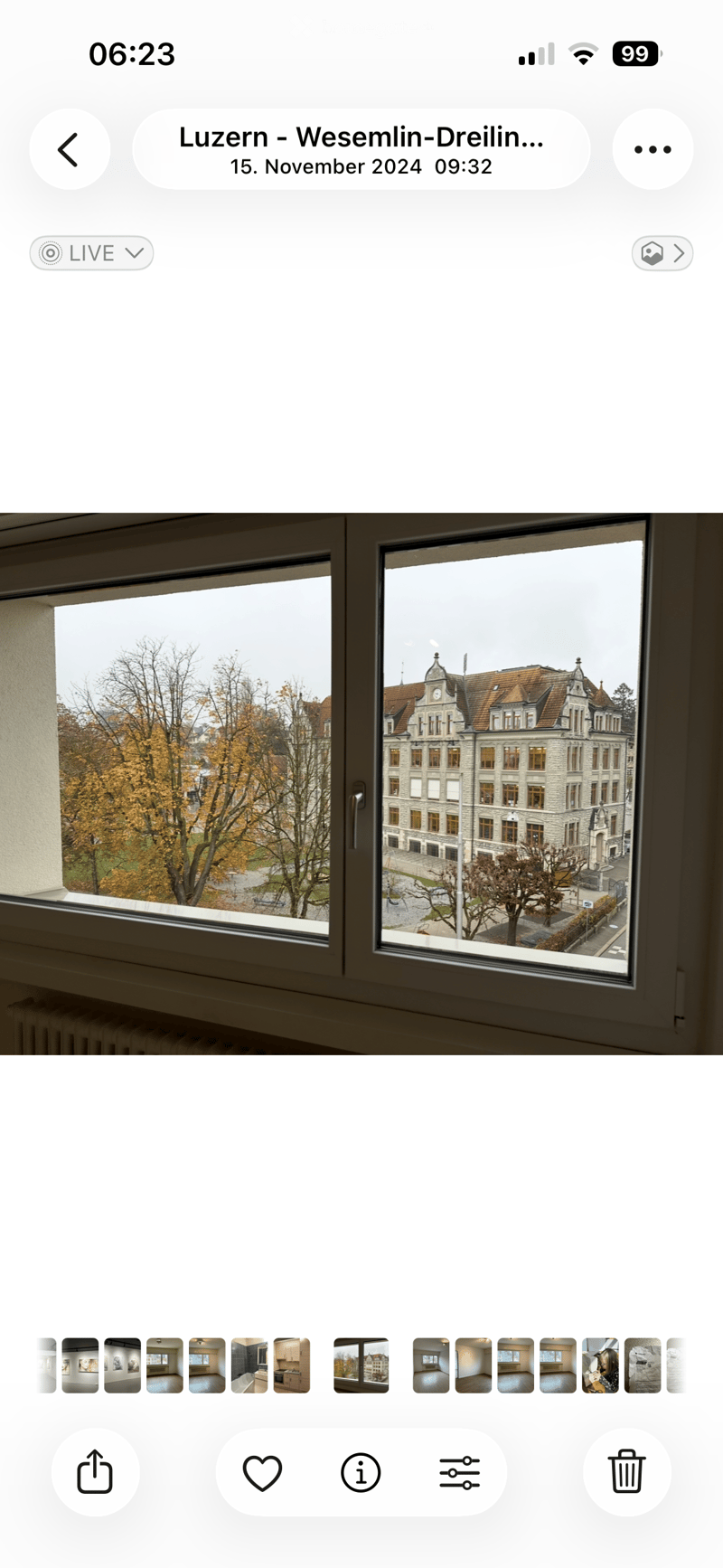 View from a window showing a historic building with a red-tiled roof and trees in the foreground.