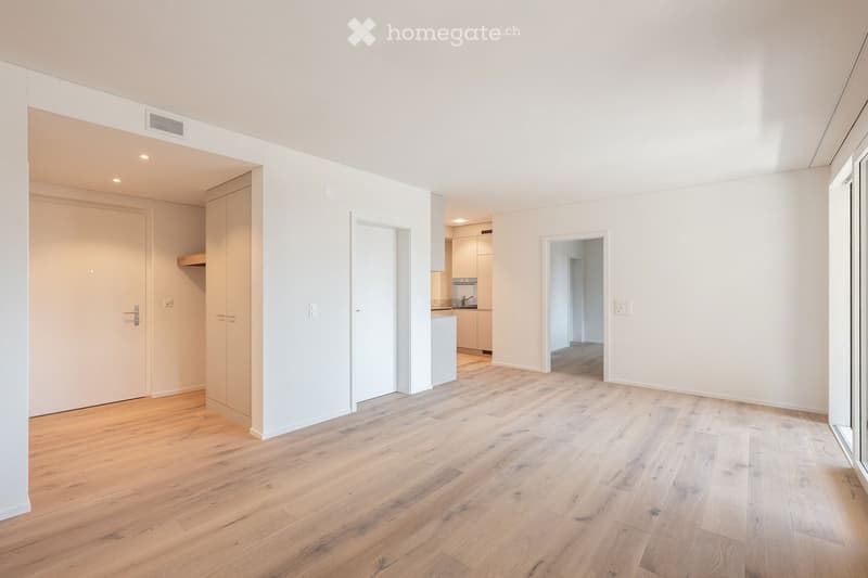 Empty room with light wooden flooring, white walls, and several doors leading to other spaces. No furniture or personal items are present.