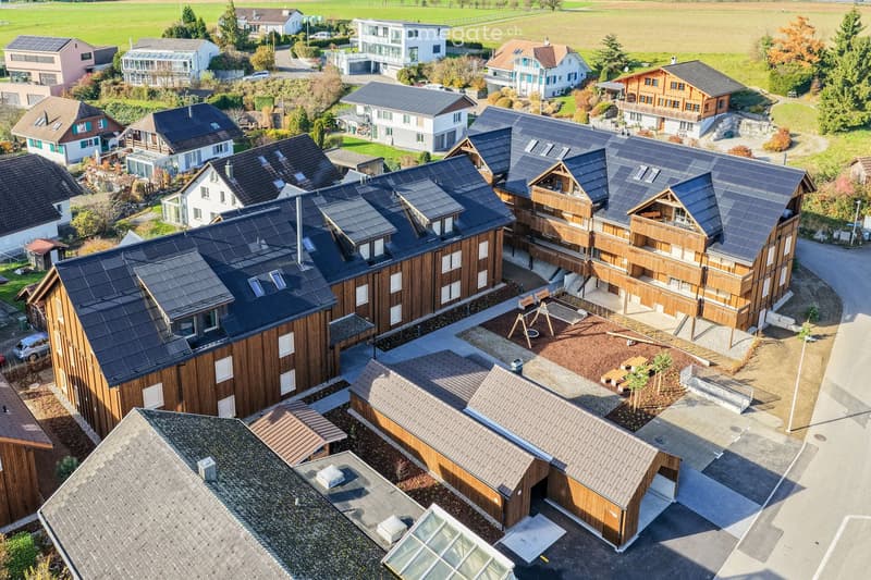 Aerial view of a residential complex with multiple houses, solar panels on roofs, and a central courtyard with playground equipment.