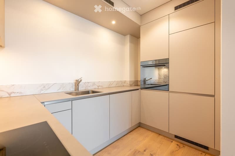 Modern kitchen with white cabinets, marble backsplash, stainless steel sink and faucet, and built-in oven.