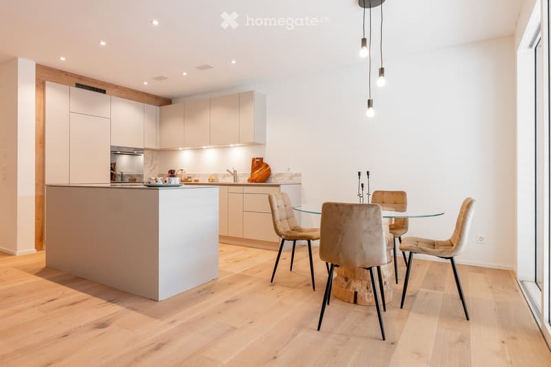 Modern kitchen with light-colored cabinets, a central island, and a dining area featuring a glass table and four chairs.
