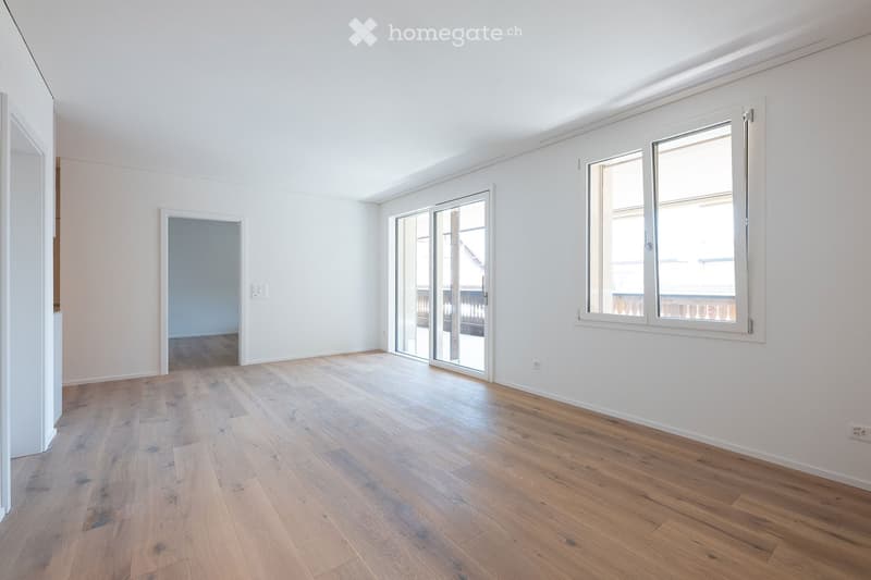 Empty room with light wooden flooring, white walls, large windows, and a sliding glass door leading to a balcony.