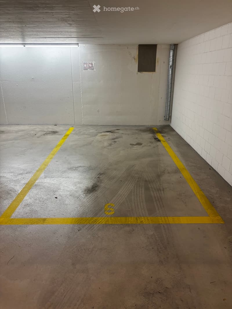 Empty underground parking space with concrete floor, yellow parking lines, and white brick walls.