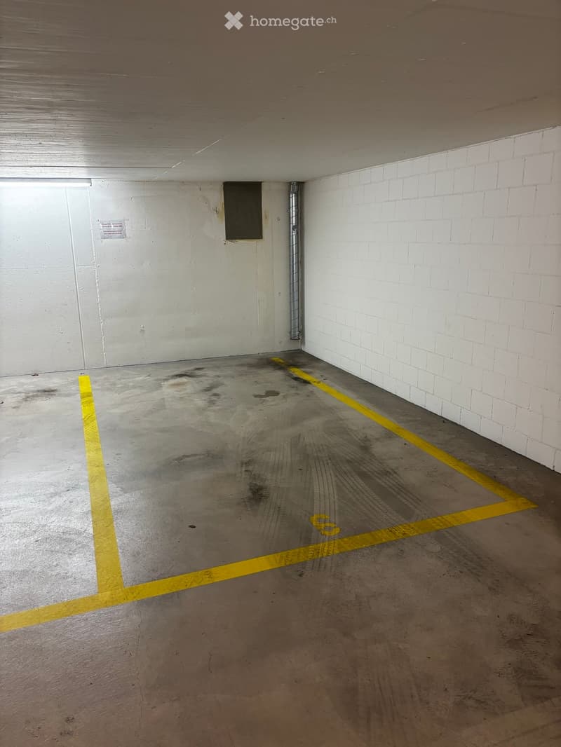 Empty underground parking space with concrete floor, white brick walls, and yellow parking lines.