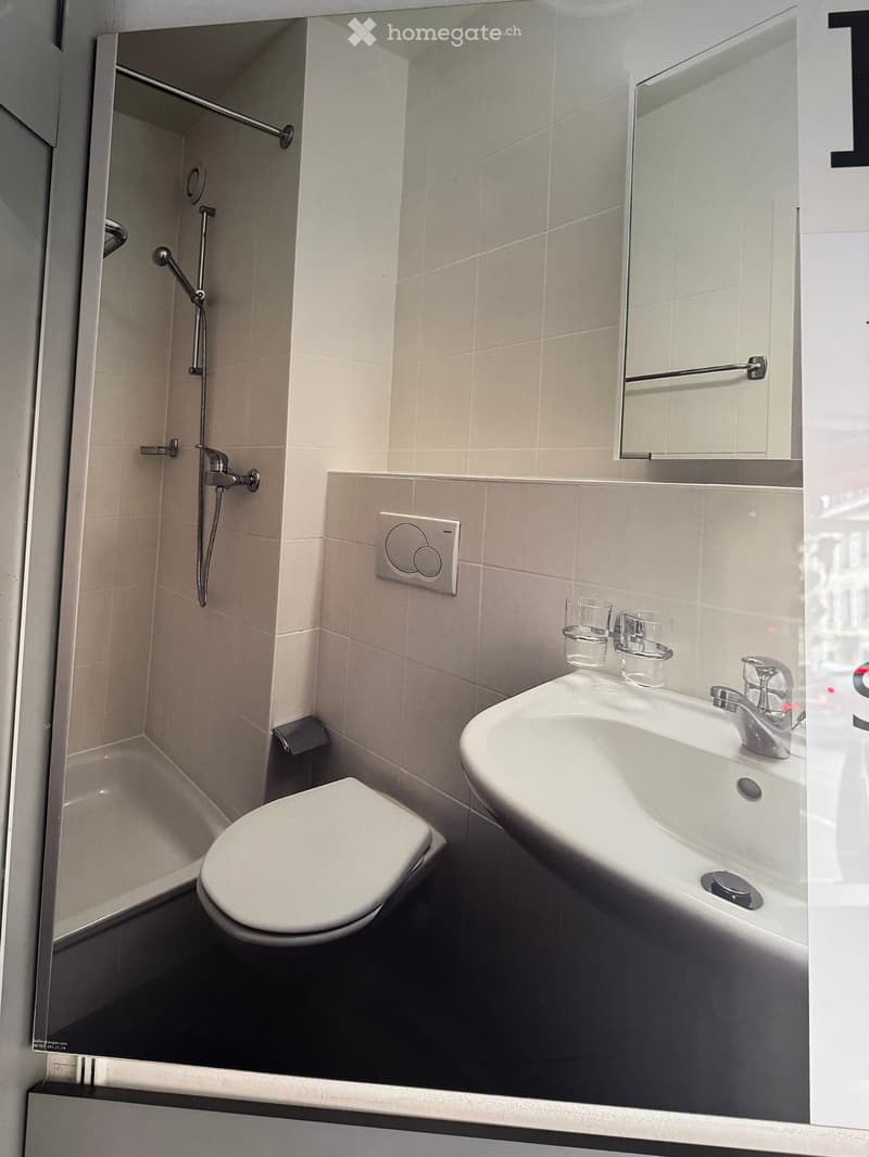 Modern bathroom with a toilet, sink, mirror, and shower area. Includes a modern faucet and two cups on the sink counter.