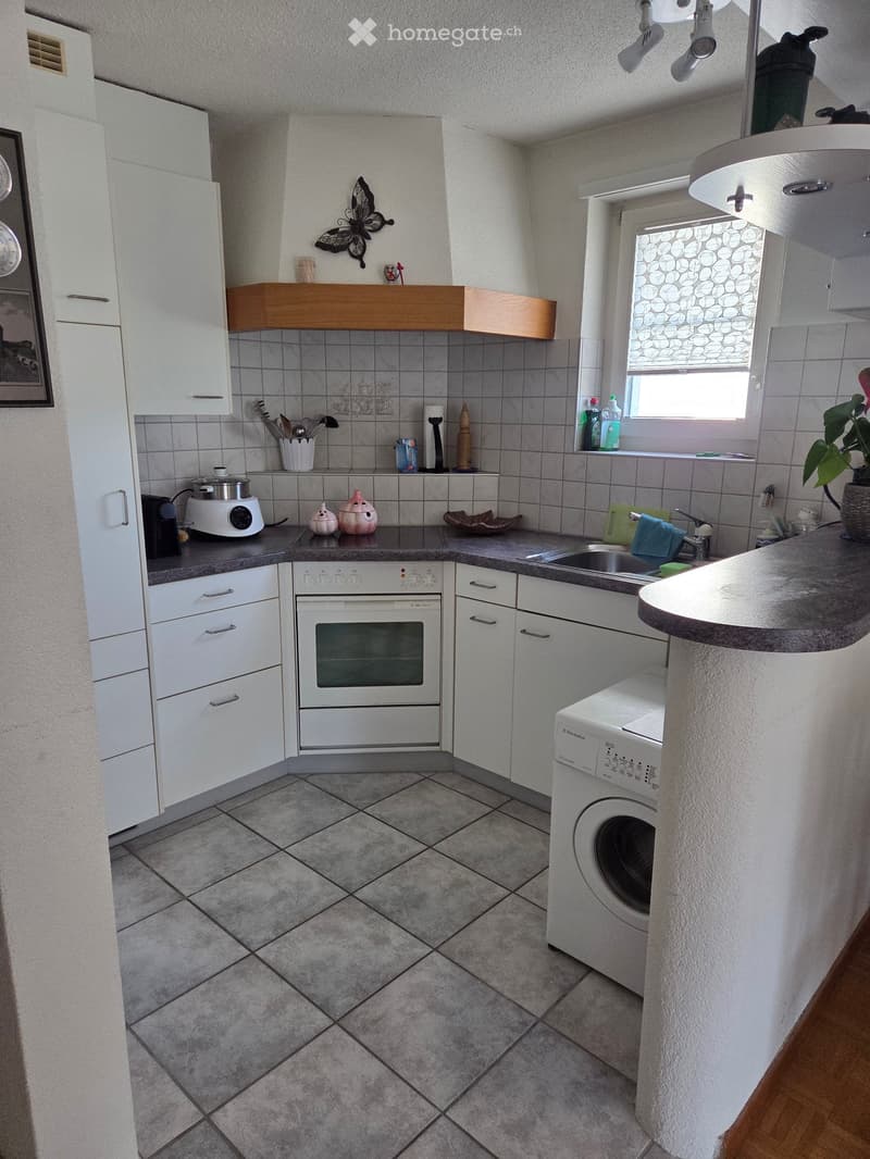 Modern kitchen with white cabinets, grey tiled floor, and various appliances including an oven, washing machine, and sink.